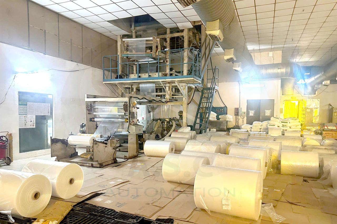 Máy thổi màng nilon đang vận hành trong xưởng, bên cạnh các cuộn màng thành phẩm